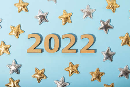 Top view of the wooden numbers 2022 on blue background.Golden and silver stars around.Festive...