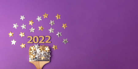 Wooden brush on the violet background with numbers 2022 above. Golden and silver stars around....