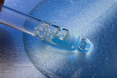Macro photography of the glass pipette in the liquid cosmetic gel. Blue background.の写真素材