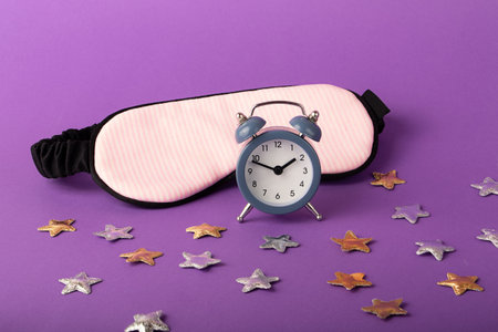 Mask for sleep and alarm clock near it.Gold and silver stars around.Circadian rhythms concept.