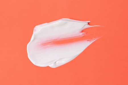 Smear of white cosmetic cream on the orange background,abstract form.の写真素材