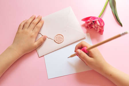 Top view of hands of anonymous child holding pink envelope with gift certificate and tulipnear...