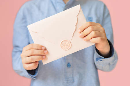 Anonymous child holding pink envelope with gift certificate in his hands.Mother day concept or wedding invintation.の写真素材