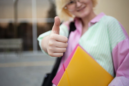 Happy sdudent showing thumb up and holding her folders.Back to school,college concept.の写真素材