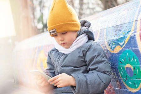 Cute child sitting outdoor and using smartphone.の写真素材