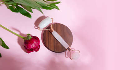 Top view of facial roller for massage on wooden slice.Pastel pink color,eco friendly concept.の写真素材