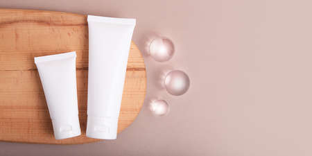 Top view of blank cosmetic tubes on wooden slice with glass spheres near.Earth tones,eco friendly concept,banner with copy space.の写真素材