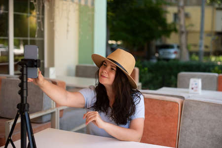Attractive smiling woman outside sitting with tripod and smartphone,making video call or providing online lesson.の写真素材