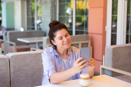 Smiling woman with smartphone and coffee cup outside.の写真素材