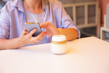 Anonymous woman with smartphone in hands and coffee cup near her.の写真素材