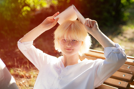 Cheerful teenage girl reading book outside,sunlight on background.の写真素材