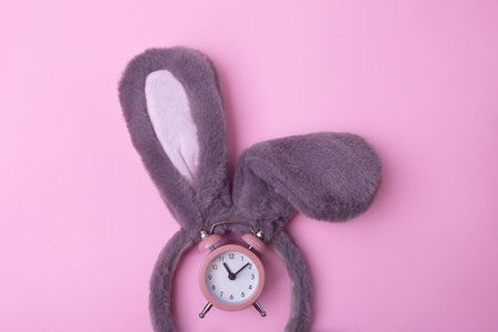 Top view of fluffy bunny rabbit ears on pink background with clock. Easter minimal concept.の写真素材