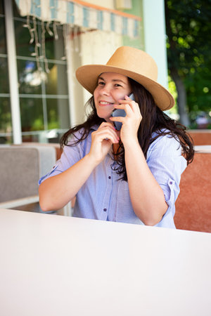 Stylish woman in hat with smartphone outside, making video call and smile.の写真素材