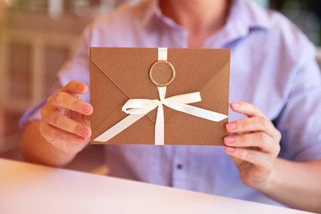 Closeup photography of woman,holding bronze invitation envelope with wax seal and satin ribbons.Sunny day.の写真素材
