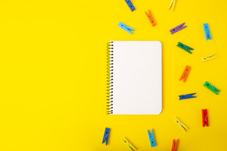 Top view of blank notebook on yellow background with multicolored decorative clothespins around.の写真素材