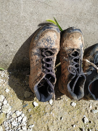 After an exhilarating trek, these muddy hiking shoes are set down, showing the wear and tear of nature's elements under a bright sky.の写真素材
