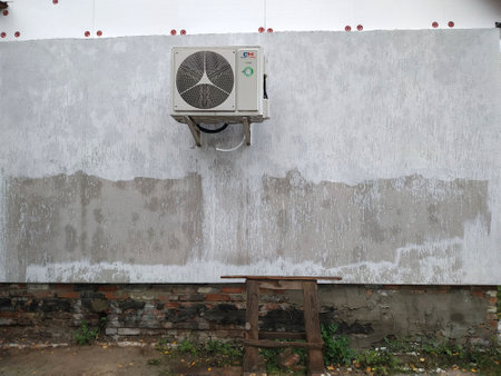 An air conditioning unit is mounted on a partially finished wall, exposing raw concrete textures below, surrounded by a natural setting and a wooden support structure.の写真素材
