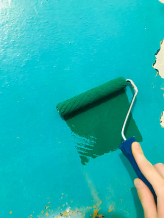 A hand rolls bright green paint on a wall indoors.の写真素材