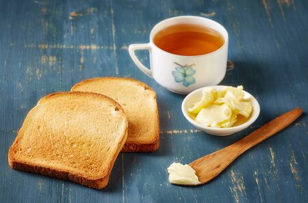 Slices of toast bread, butter and tea on blue wooden tableの写真素材