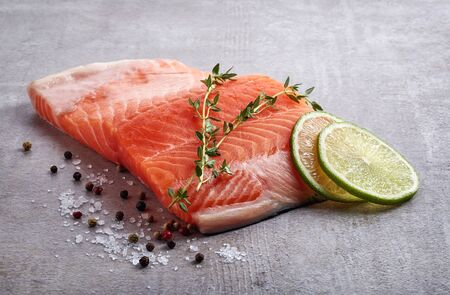 Fresh raw salmon fillet with lime, rosemary, pepper and salt on grey table