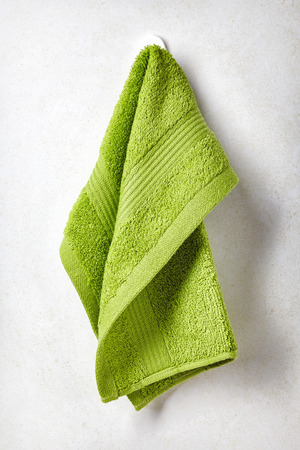 Green spa towel hanging on white bathroom wall backgroundの写真素材