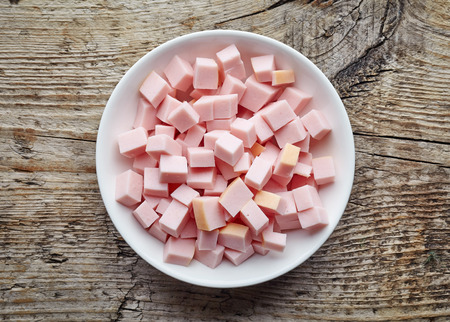 White bowl of chopped ham sausage on wooden table, top viewの写真素材