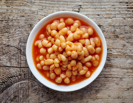 White bowl of beans in tomato sauce on wooden table, top viewの写真素材