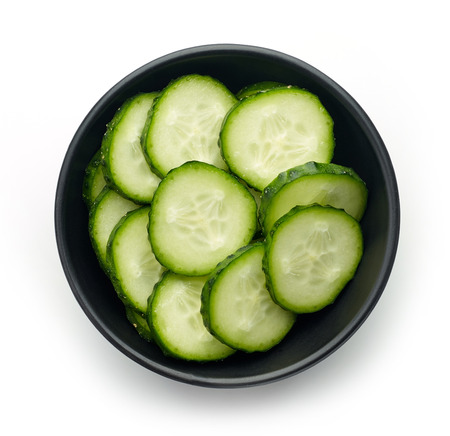 Black bowl of fresh cucumber slices isolated on white background, top viewの写真素材