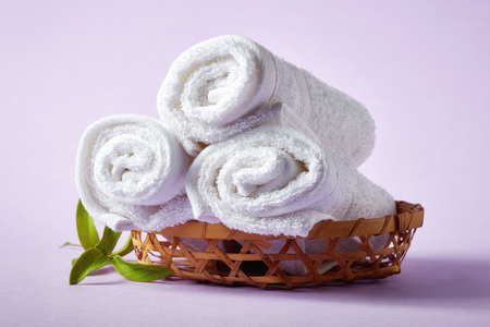White spa towels in wicker basket on light purple background, top viewの写真素材