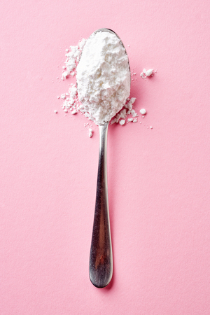 Spoon with powder sugar isolated on pink background, top viewの写真素材