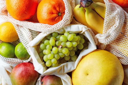 Fresh fruits in cotton bags, eco friendly and zero waste shopping concept, bananas, oranges, limes, lemons, grapes, mangos and pomelo from marketの写真素材