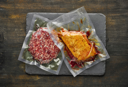 Duck breast and burger meat vacuum sealed ready for sous vide cooking on wooden table, from above