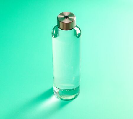 Reusable glass water bottle with stainless steel cap on mint green background