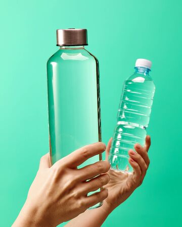 Zero waste concept - reusable glass water bottle vs single use plastic bottle on mint green backgroundの写真素材