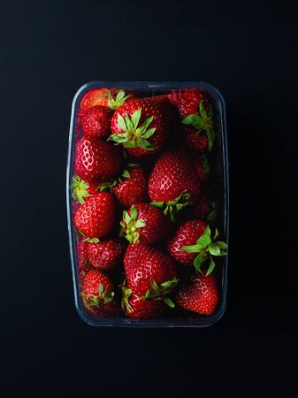 Strawberries in plastic transparent container box on black background, top viewの写真素材
