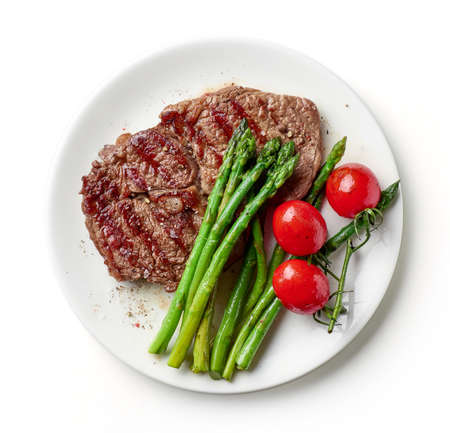 Grilled entrecote, asparagus and tomatoes on white plate isolated on white background, top viewの写真素材