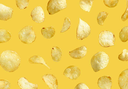 Salted potato chips flying in the air on yellow backgroundの写真素材