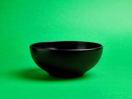 Empty black ceramic bowl on green backgroundの写真素材