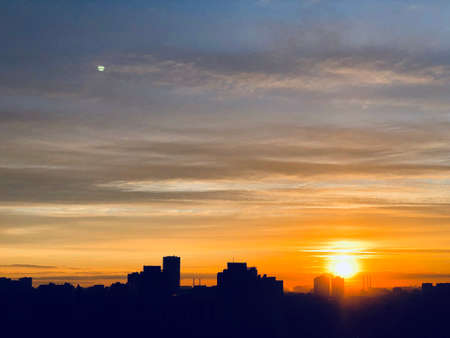 City skyline, silhouette against sky with clouds, sun and moon on a sunset, dawn. City skyline, skyscraper silhouettes with sunset sky on the backgroundの写真素材