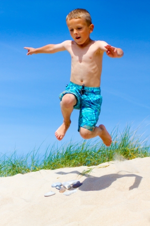 Young Caucasian boy is having fun doing wild jumps in sand dunes  Boy is wearing bright blue swim shorts の写真素材