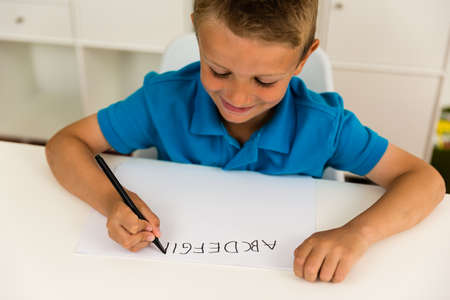 Young caucasian boy writing letters on a white piece of paper.の写真素材