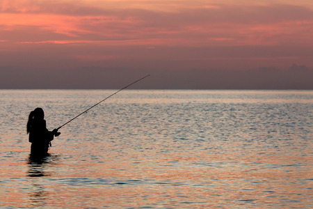 Solitary fisherman waiting for the next catch with the faded sun hovering on the horizon.の写真素材