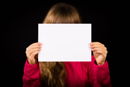 Studio shot of girl holding a blank sign made of white paper. Focus on sign. Girl is blurred.の写真素材