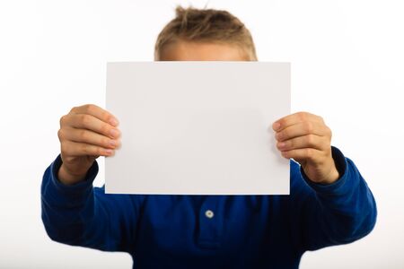 Studio shot of boy showing blank white sign with plenty of copy space. Focus on sign. Boy is blurred.の写真素材