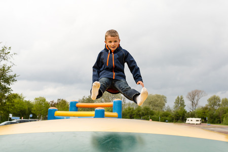 Young child jumping on bouncing trampoline at playground on a cloudy day.の写真素材