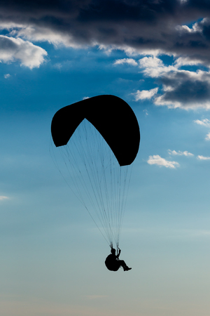 Silhouette of man with parachute with dark blue skies in the background.