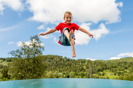 Young Scandinavian boy playing and having fun while jumping up and down on inflatable bouncing trampoline.の写真素材