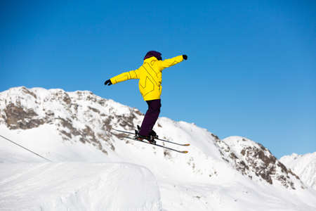 Skier performing a jump trick in ski resort on a sunny winter day.の写真素材