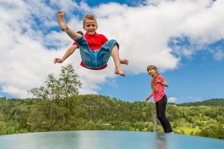 Two scandinavian children playing and having fun while jumping on large inflatable bouncing trampoline.の写真素材