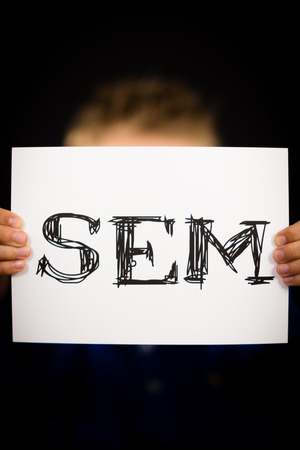 Studio shot of child holding a SEM sign made of white paper with handwriting.の写真素材